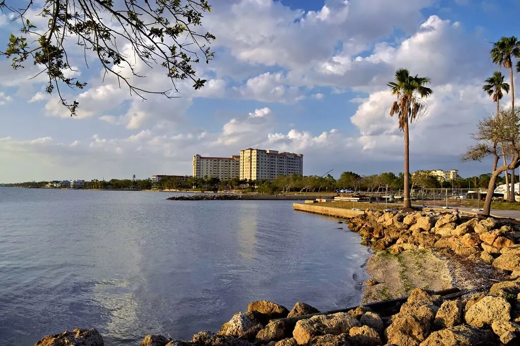 Peaceful waterfront condos in Sarasota with palm trees, rocks, and blue sky.